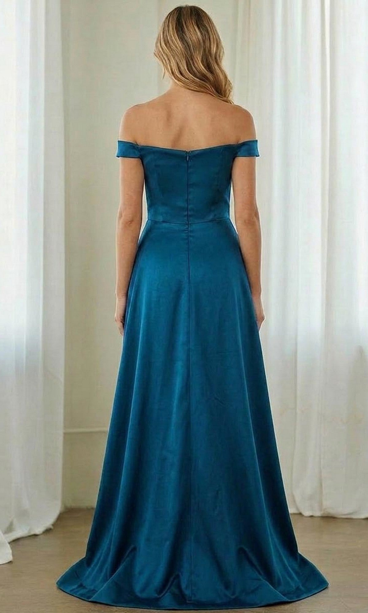 A woman stands with her back to the camera in a room with white curtains, wearing the Long Formal Dress: Amelia Couture 7094 in teal, featuring an elegant off-the-shoulder design.